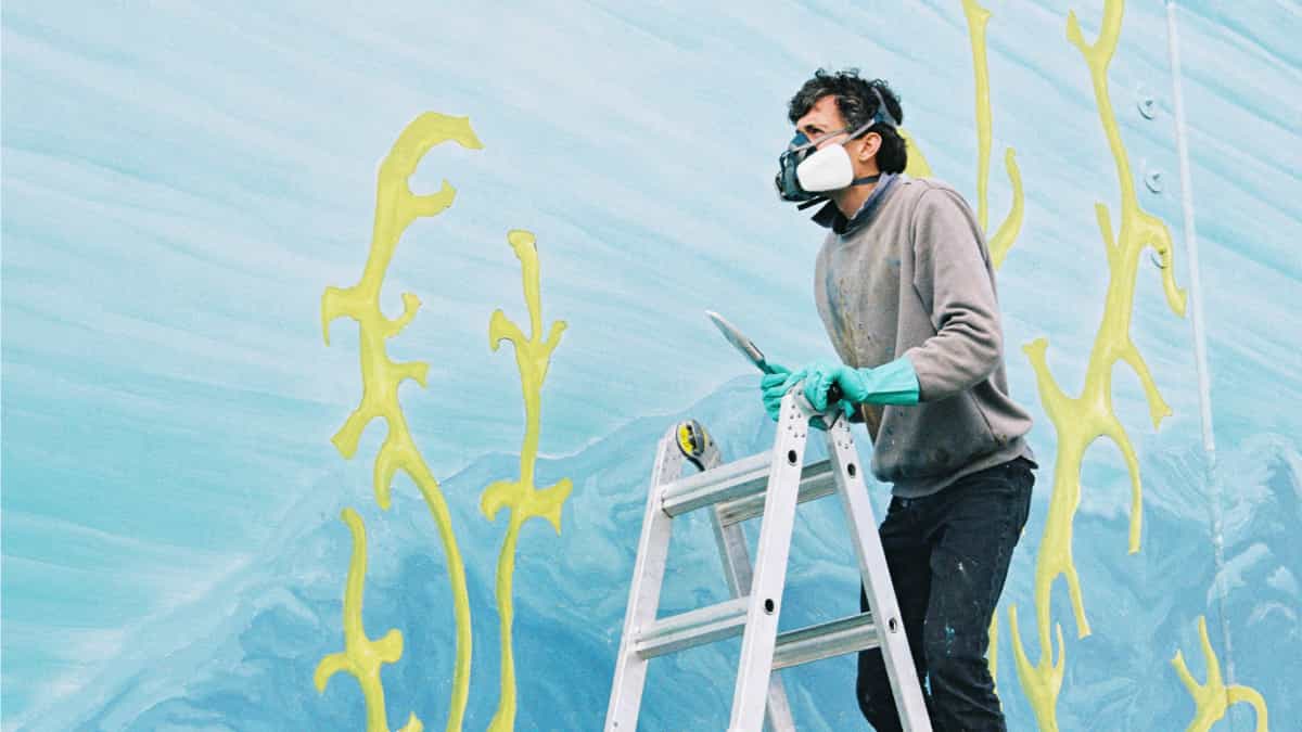 WA-based mural artist, Tom Ansell at work, mounted on a ladder.